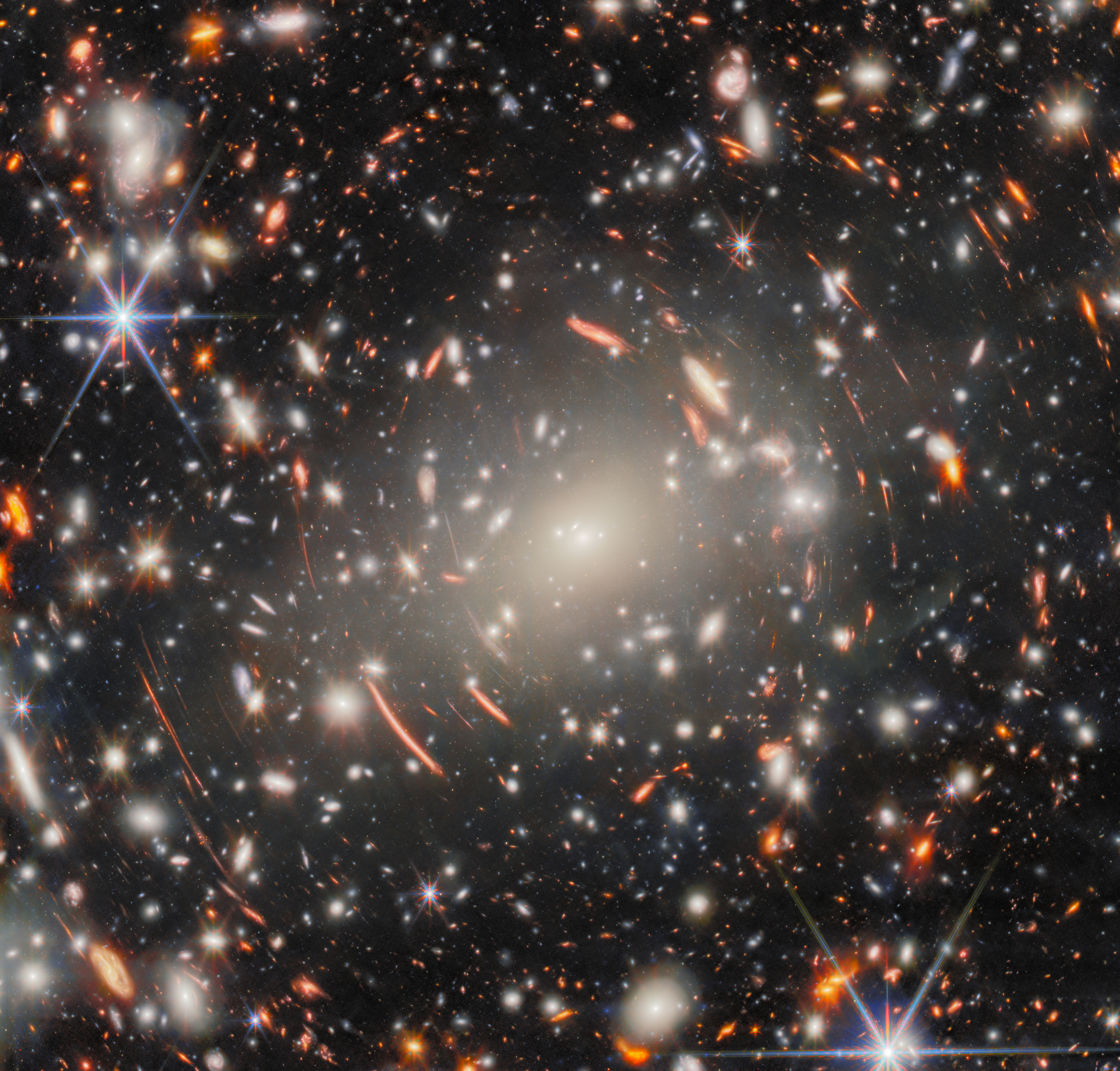 A dense cluster of distant galaxies with bright stars and curved light patterns in space, captured by JWST, shows some of the most extreme gravitational lens effects ever observed.