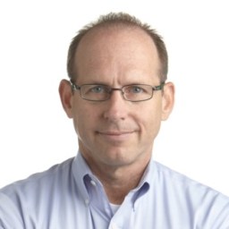 A middle-aged man with short hair, glasses, and a light blue collared shirt looks directly at the camera against a plain white background.