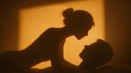 Silhouettes of two people face each other closely, with warm light casting their shadows on a wall.