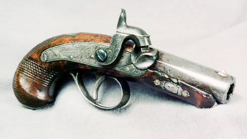 An antique percussion cap pistol with an engraved metal barrel and wooden handle, displayed on a neutral background.