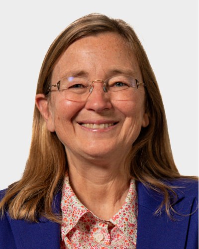 Kim Scott, best seller author, wearing a blue blazer and a floral shirt, smiling at the camera against a plain background.