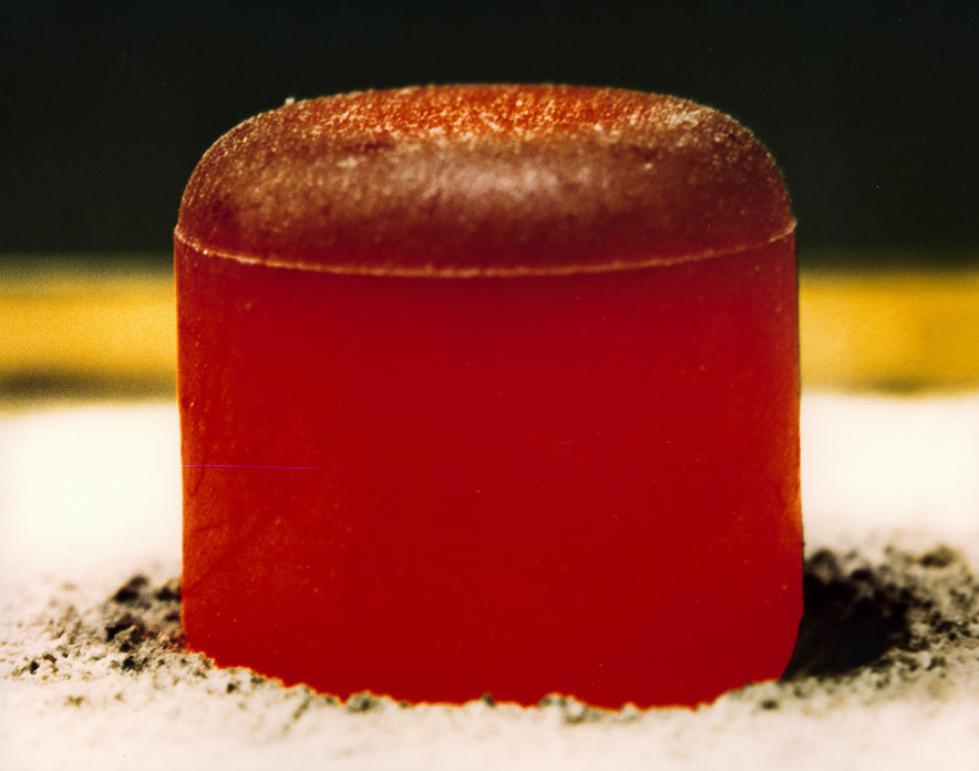 A close-up of a cylindrical, reddish-brown solid object with a rounded top, resting on a surface dusted with dark powder—resembling something you might find during a mission to Uranus or Neptune.