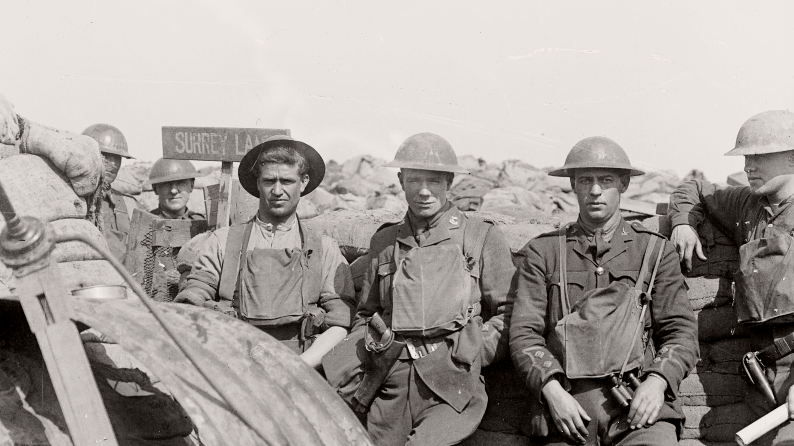Five World War I soldiers in uniform stand and sit near sandbags in a trench, with a sign reading "Surrey Lane" visible in the background—evoking camaraderie amid the Ring of Fire on the front lines.