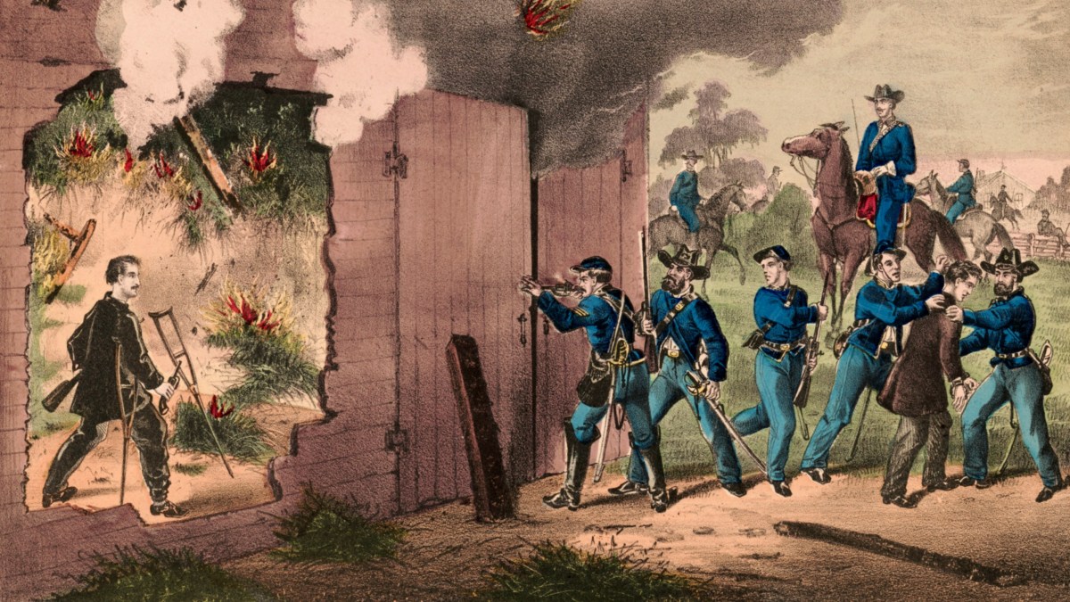 Union soldiers in blue uniforms escort prisoners past a burning building with a large hole in the wall while smoke and flames rise, during the American Civil War.