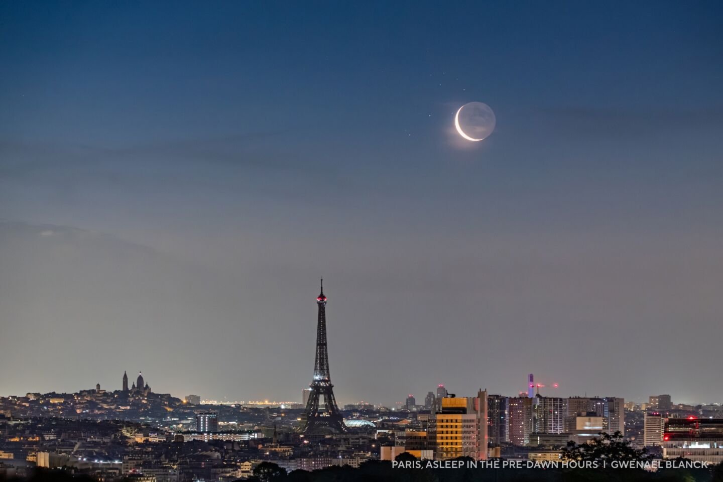 A pre-dawn view of Paris with the Eiffel Tower in the center, city lights twinkling, and a crescent moon rising—perfect for 2025 night sky images.