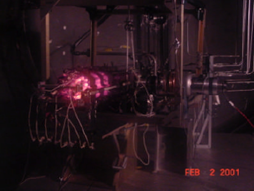 A laboratory setup features electronic equipment and wires, with a glowing pink light source in the center—resembling a miniature nuclear reactor; the date stamp reads "FEB 2 2001.
