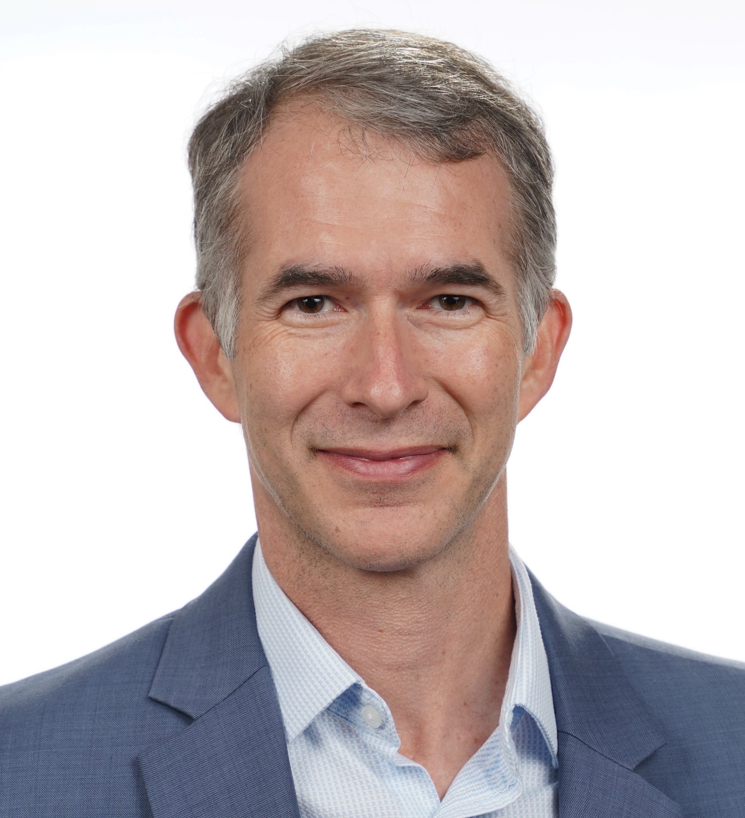 A middle-aged man with short gray hair, wearing a blue blazer and light blue shirt, smiling at the camera against a plain white background.
