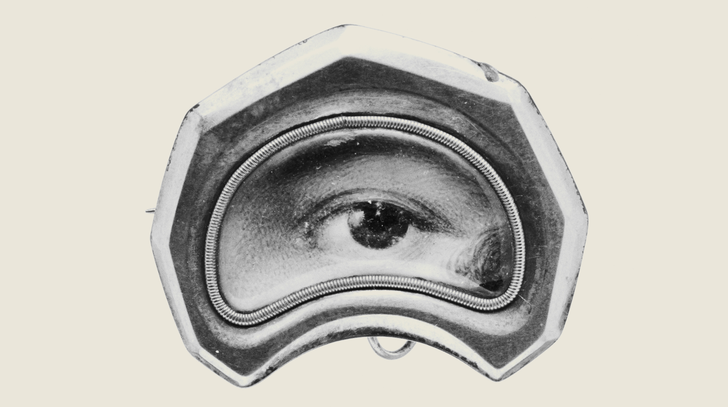 A vintage, hexagonal brooch featuring a realistic painted human eye in the center, surrounded by a metallic frame.