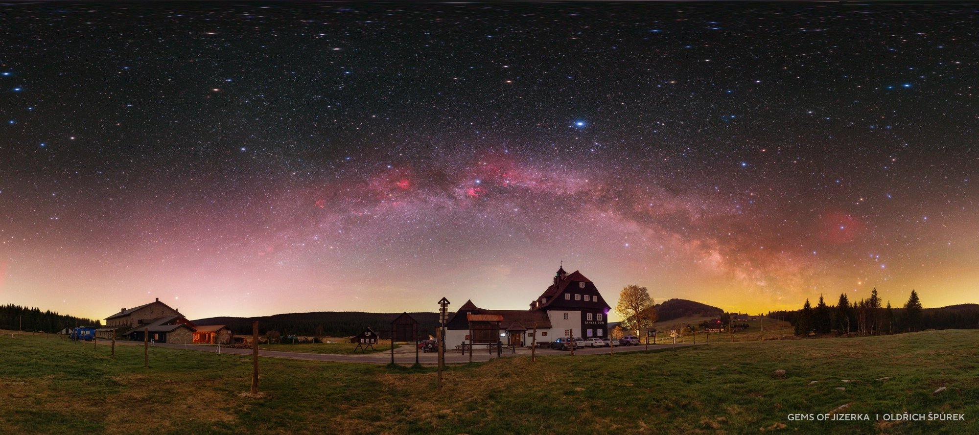 A wide field view of rural houses under a clear night sky features the Milky Way arching brightly overhead, reminiscent of 2025 night sky images with countless stars visible above the horizon.