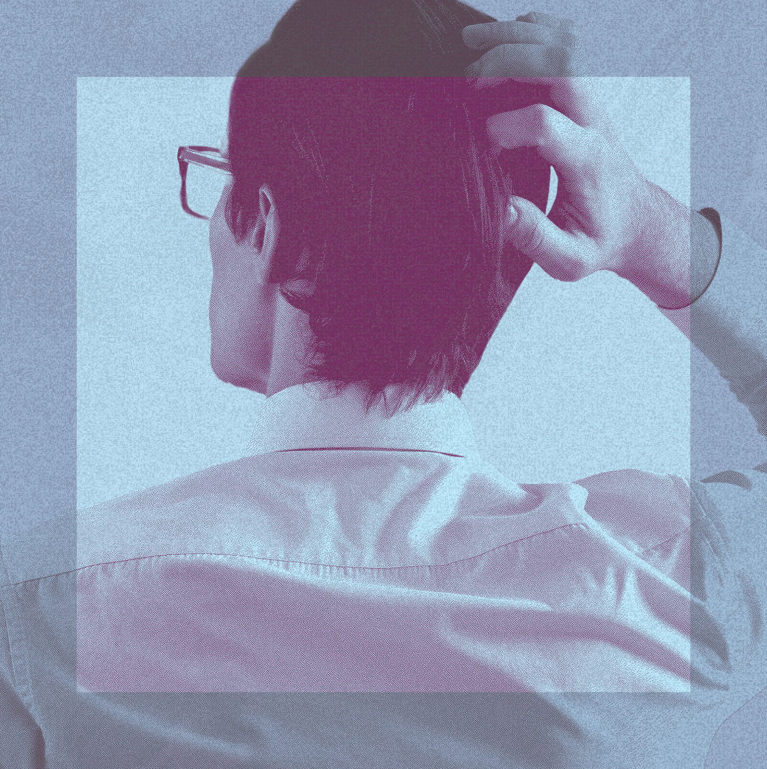 A person with short brown hair, wearing glasses and a collared shirt, is seen from behind with one hand adjusting their hair.