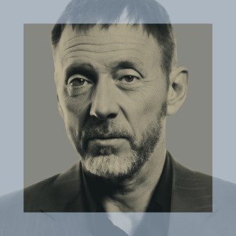 A middle-aged man with short hair and a beard, wearing a suit jacket, looks directly at the camera. The image has a transparent overlay framing his face.