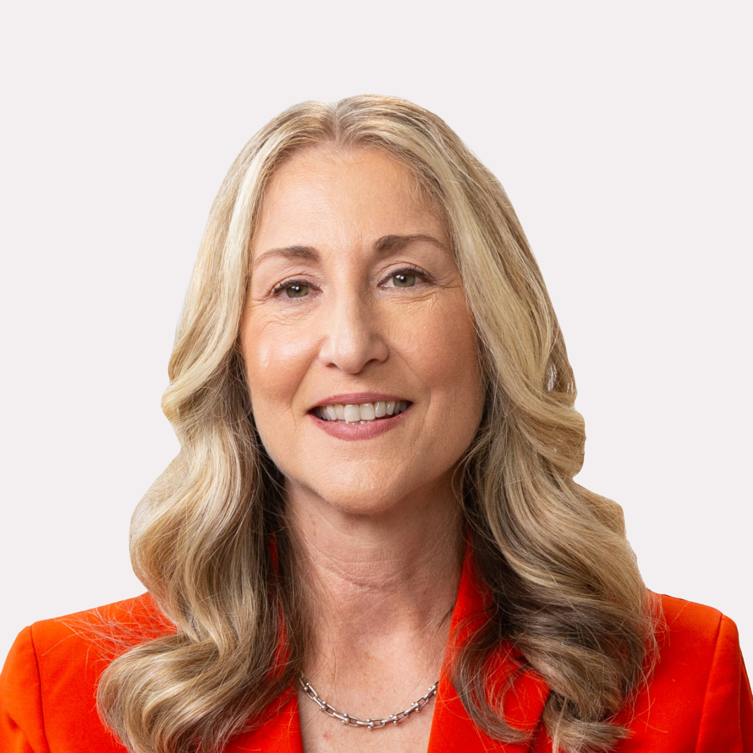 A woman with long blonde hair wearing a bright orange blazer and a silver necklace, smiling at the camera against a plain light background.