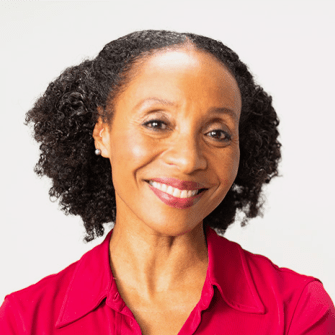 A woman with curly black hair, wearing a red collared shirt, smiles at the camera against a plain white background.