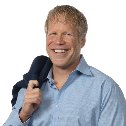 Smiling man with blond hair in a light blue button-down shirt holds a dark jacket over his shoulder against a white background.