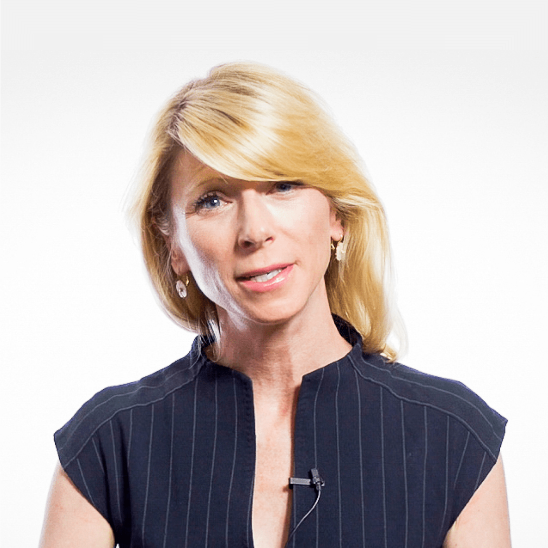 A woman with blonde hair, wearing a black, short-sleeved, pinstriped top and a lapel microphone, stands against a plain white background.