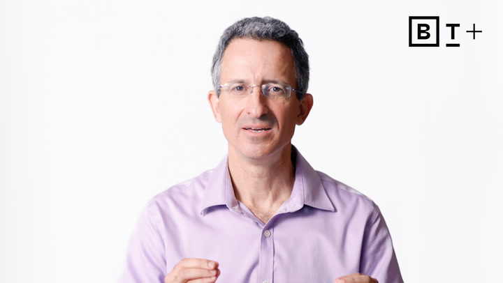 A middle-aged man wearing glasses and a light purple shirt stands against a white background with a "B T +" logo in the top right corner.