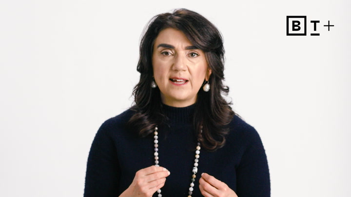 A woman with dark hair wearing a black sweater and beaded necklace speaks against a plain white background with a "B T +" logo in the top right corner.
