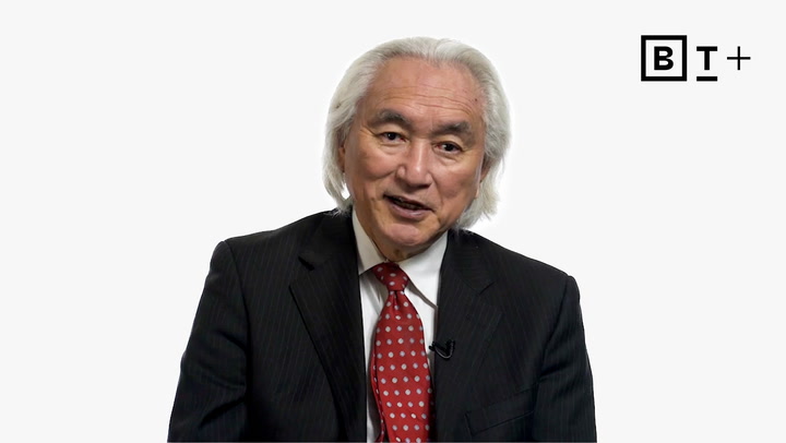 An older man with white hair, wearing a black suit, white shirt, and red tie, sits in front of a white background with the B+ logo in the top right corner.