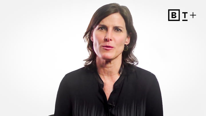 A woman with shoulder-length dark hair in a black blouse sits against a white background with a "B T +" logo in the top right corner.