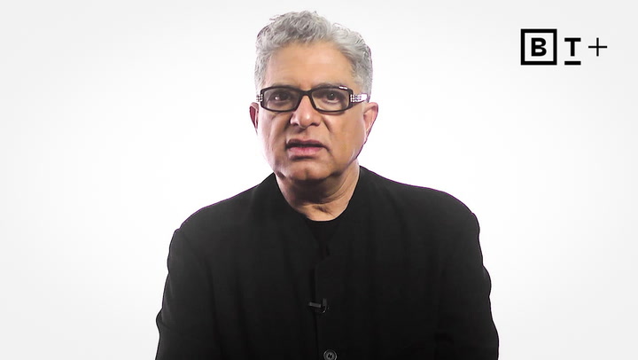 A man with gray hair and glasses wearing a black jacket is speaking in front of a white background with the B+ logo in the top right corner.