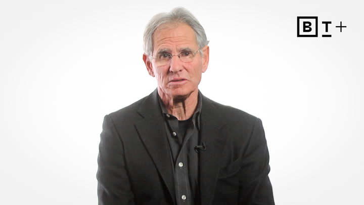 An older man with gray hair and glasses wears a dark suit and looks toward the camera; a black and white "BT+" logo appears in the top right corner.