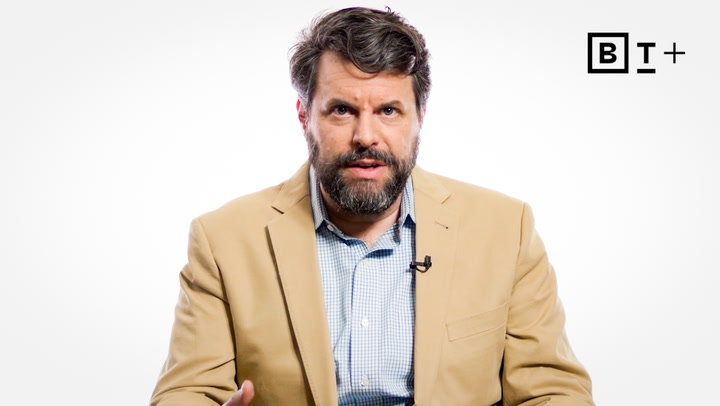 A man with a beard wearing a tan blazer and blue shirt speaks while seated against a plain white background with a "BT+" logo in the top right corner.