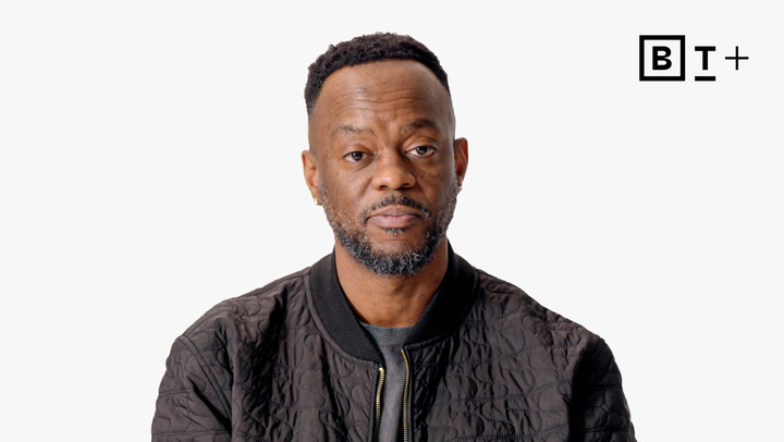 A man with a short beard and close-cropped hair wears a black jacket, looking at the camera against a plain white background with a "B T +" logo in the top right corner.