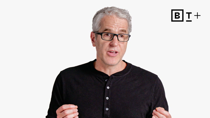 A middle-aged man with gray hair and glasses speaks while gesturing with his hands, wearing a black shirt. A "BT+" logo is visible in the top right corner.