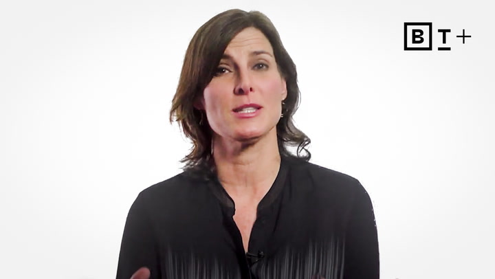 A woman with shoulder-length brown hair wearing a black blouse speaks in front of a white background with a "BT+" logo in the upper right corner.