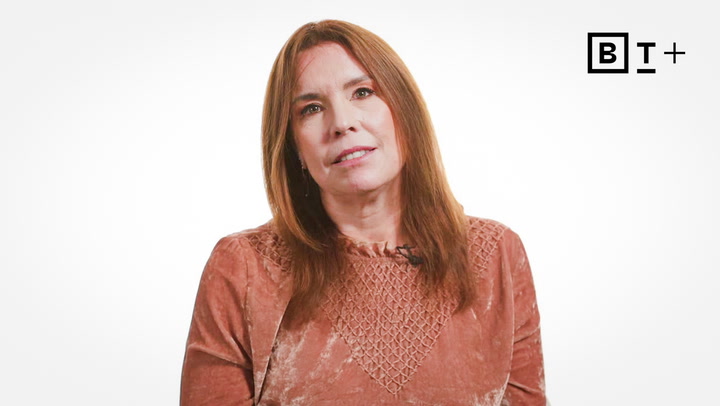 A woman with straight brown hair wearing a textured, light brown top sits in front of a plain white background with a "BT+" logo in the top right corner.