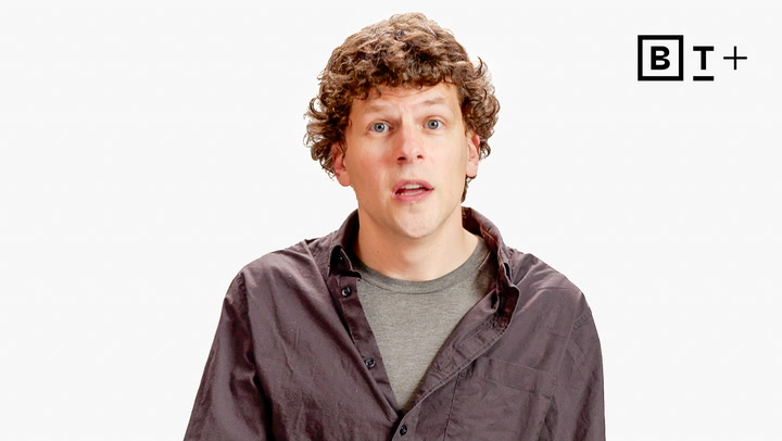 A man with curly hair wearing a gray t-shirt and dark button-up shirt stands in front of a plain white background with a "B T +" logo in the corner.