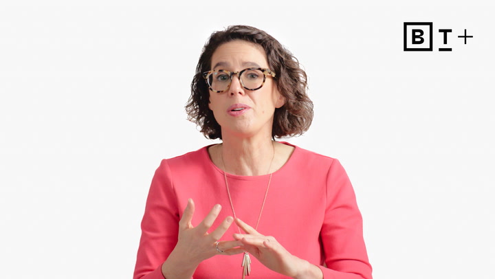 Woman with curly hair and glasses wearing a pink top speaks and gestures with her hands; BT+ logo in the top right corner.