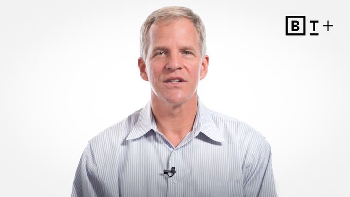 A man in a striped shirt sits in front of a plain white background with a BT+ logo in the top right corner.