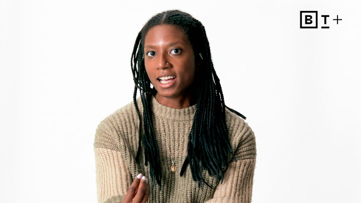 A person with long braided hair wearing a beige sweater speaks while gesturing, against a plain white background with a "BT+" logo in the top right corner.