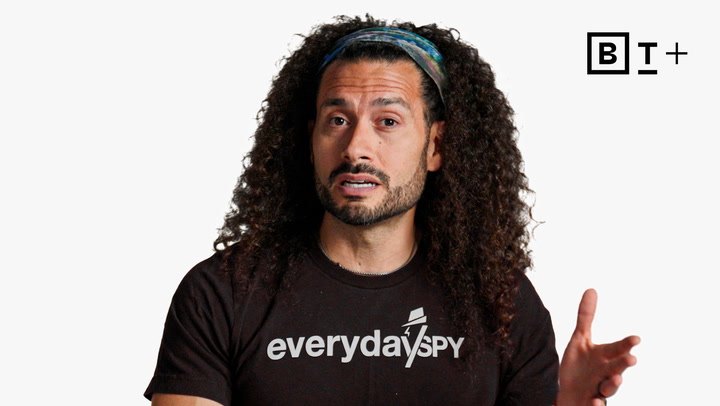 A man with long curly hair and a headband speaks, wearing an "everyday spy" T-shirt. A BT+ logo is in the top right corner against a plain white background.