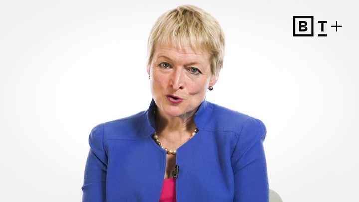 A woman with short blond hair wearing a blue blazer and pearl necklace speaks in front of a plain white background with a "BT+" logo in the top right corner.