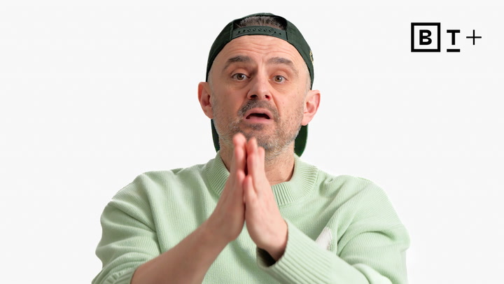 Man in a light green sweater and backward cap holds his hands together, speaking with a neutral expression; "B T +" logo is visible in the upper right corner.