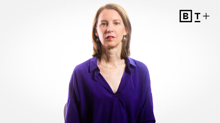 A woman with straight, shoulder-length brown hair wearing a purple blouse sits in front of a plain white background with a "B T +" logo in the top right corner.