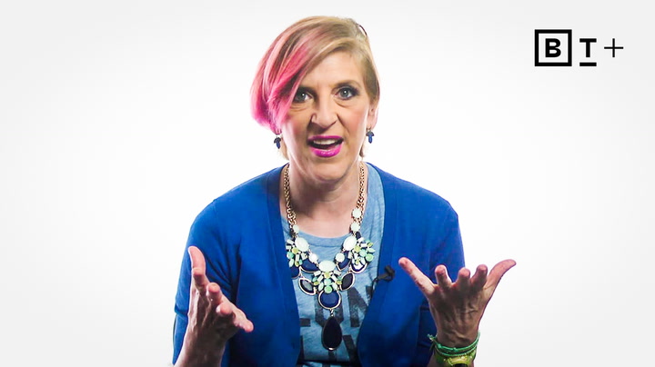 A person with short, partially pink hair and a blue outfit gestures with both hands while speaking, sitting against a plain white background with a "BT+" logo in the corner.