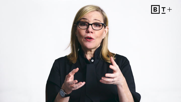 A woman with blond hair and glasses speaks while gesturing with her hands, against a plain white background with a BT+ logo in the top right corner.