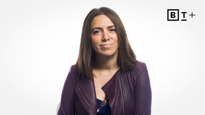 A woman with straight brown hair wears a purple jacket and sits against a plain white background with a "BT+" logo in the top right corner.