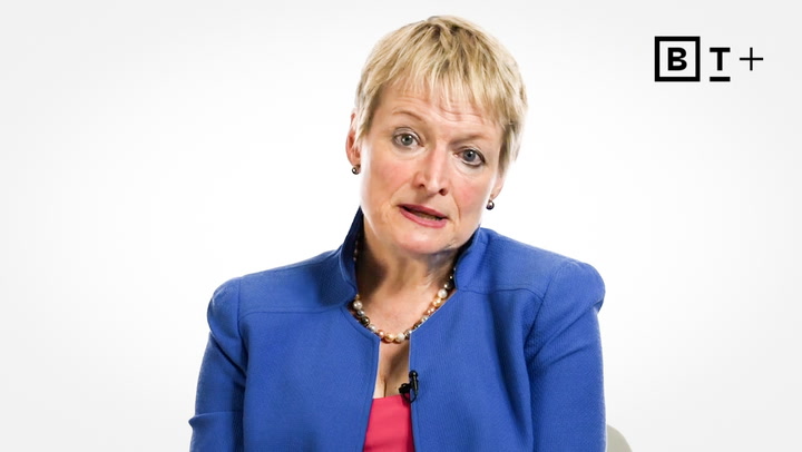 A woman with short blonde hair in a blue blazer and pink top sits against a white background with a "B T +" logo in the top right corner.