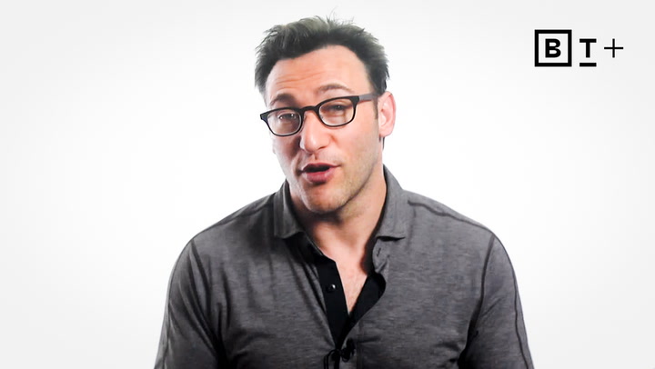 A man with dark hair and glasses wearing a gray collared shirt speaks in front of a white background with a "BT+" logo in the top right corner.