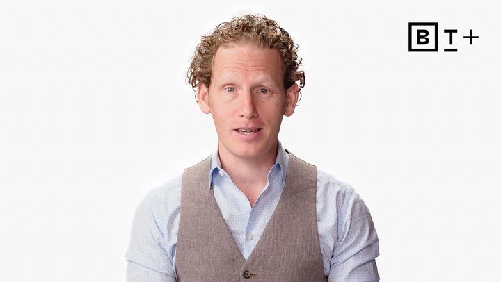 A man with curly hair wearing a light blue shirt and grey vest stands in front of a white background with a "BT+" logo in the top right corner.