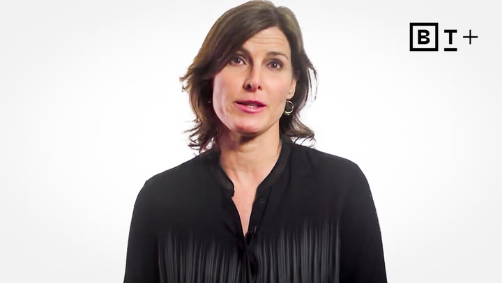 A woman with shoulder-length brown hair wearing a black blouse stands in front of a white background with a "BT+" logo in the top right corner.