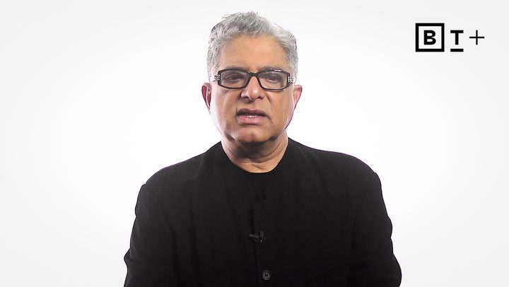 A man with short gray hair and glasses, wearing a black jacket, sits in front of a white background with a "B T +" logo in the upper right corner.