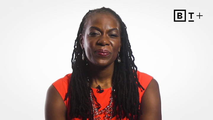 A woman with long, dark braided hair and a red top sits against a plain white background with a BT+ logo in the corner.