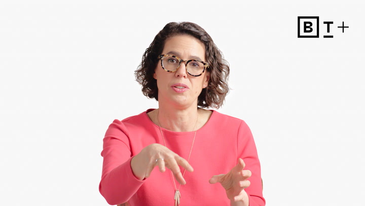 A woman with short curly hair and glasses, wearing a pink top, gestures with her hands while speaking. The BT+ logo is visible in the top right corner.
