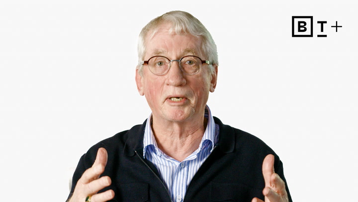 An older man with glasses speaks, gesturing with his hands. He wears a striped shirt and dark jacket. The BT+ logo appears in the top right corner against a white background.