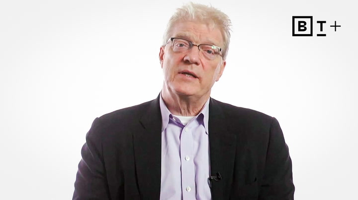 An older man with glasses and white hair wearing a suit jacket and light purple shirt sits against a plain white background with a "B T +" logo in the top right corner.